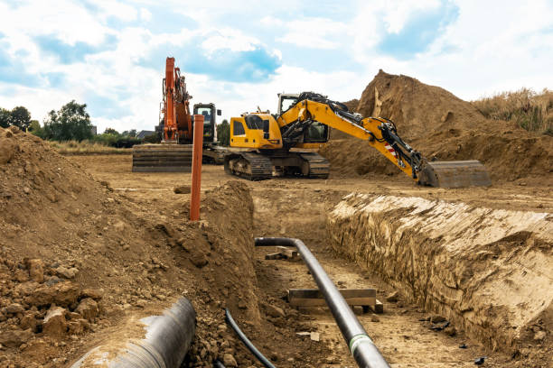 Installation of new gas pipes on a building site with a view down the open trench and heavy duty machinery and digger in the background